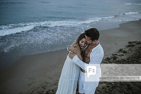 Junger Mann umarmt Frau am Strand stehend