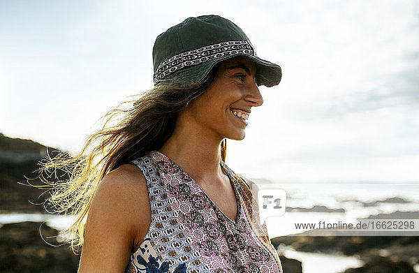 Cheerful young woman in hat looking away while spending weekend at beach
