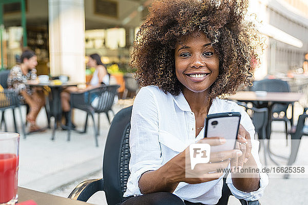 Frau  die in einem Café sitzend eine SMS auf ihrem Smartphone schreibt