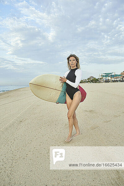 Beautiful woman carrying surfboard while standing on beach