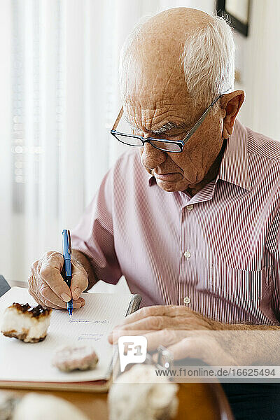 Älterer Mann im Ruhestand schreibt in ein Buch  während er mit Mineralien und Fossilien am Tisch sitzt