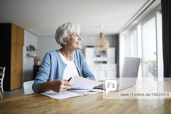 Aktive ältere Frau  die zu Hause sitzend Papierarbeiten erledigt