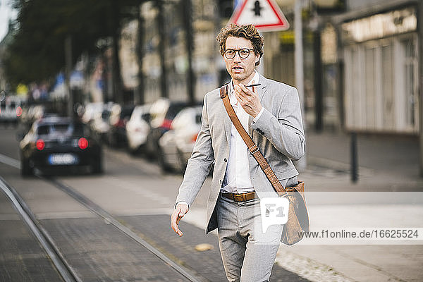 Mann mit Brille  der mit seinem Handy telefoniert  während er in einer Straßenbahn in der Stadt spazieren geht