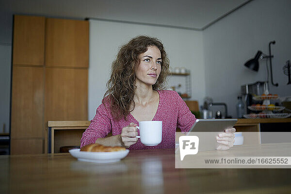 Frau beim Frühstück  während sie zu Hause ein digitales Tablet benutzt
