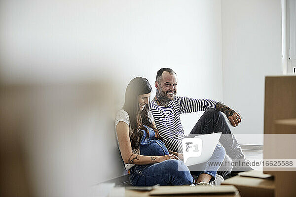 Glückliches Paar arbeitet an einem Laptop  während es in einem Hauswirtschaftsraum sitzt