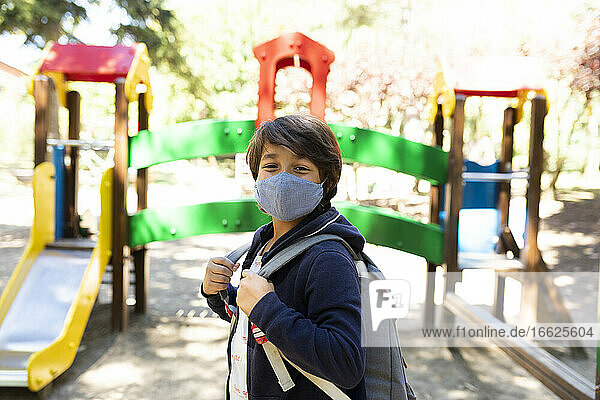 Junge mit Maske und Rucksack auf dem Schulhof