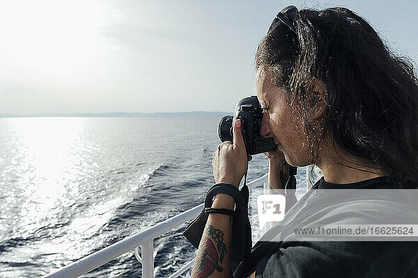 Frau  die durch eine Kamera fotografiert  während sie auf einem Passagierschiff steht