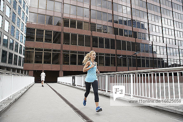 Mature blond woman jogging against businesswoman on footbridge in financial district