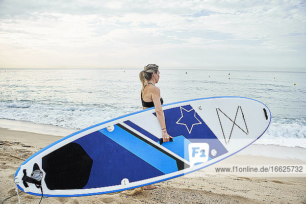 Frau geht mit Surfbrett am Strand bei Sonnenuntergang