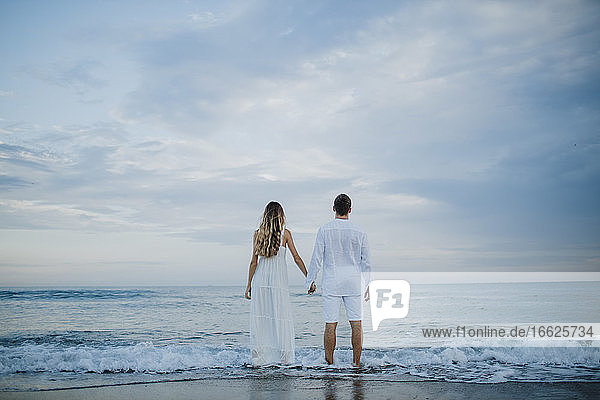 Paar hält sich an der Hand und bewundert die Aussicht am Strand am Rande des Wassers