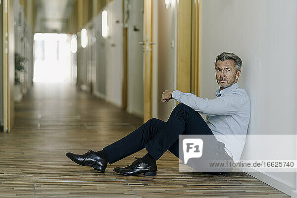 Mann auf dem Boden sitzend im Korridor eines Büros