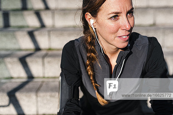 Nahaufnahme einer Sportlerin  die über Kopfhörer Musik hört  während sie auf einer Treppe sitzt