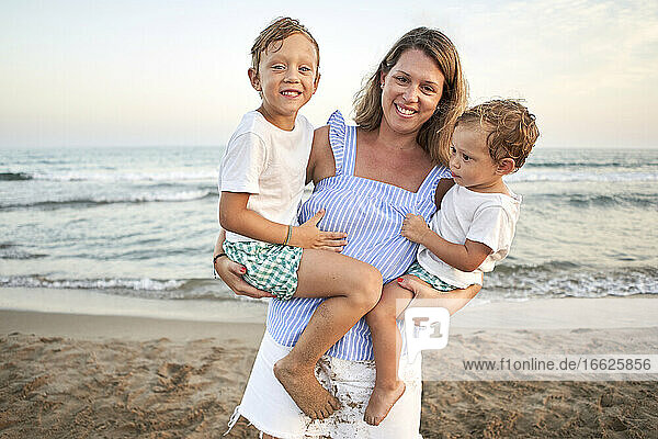 Woman carrying boys in arms while standing at beach
