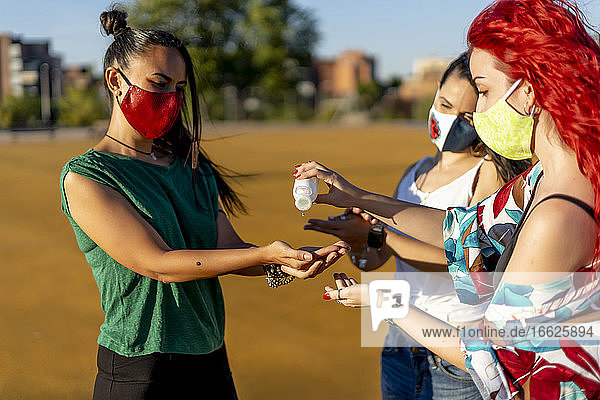Freunde benutzen Händedesinfektionsmittel  während sie an einem sonnigen Tag im Freien stehen
