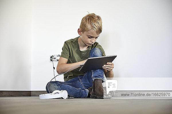 Kleiner Junge spielt auf einem digitalen Tablet  während er in einem neuen Haus sitzt
