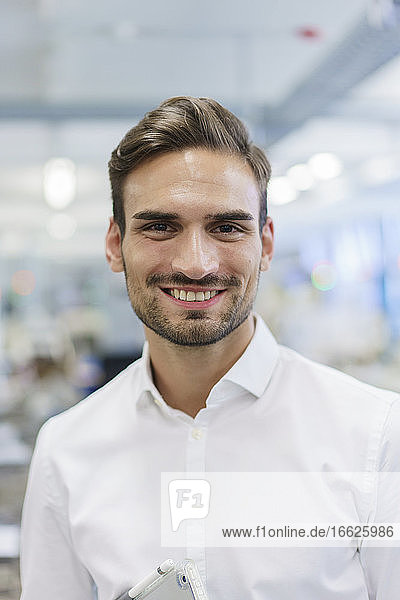 Lächelnder junger männlicher Ingenieur vor einer beleuchteten Fabrik