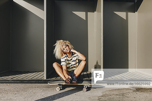 Woman with skateboard sitting against metallic cabins on sunny day