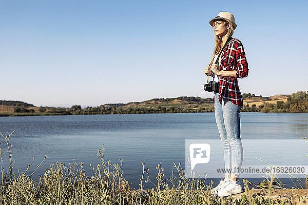 Junge Frau steht mit Kamera auf einer Stützmauer gegen den klaren Himmel