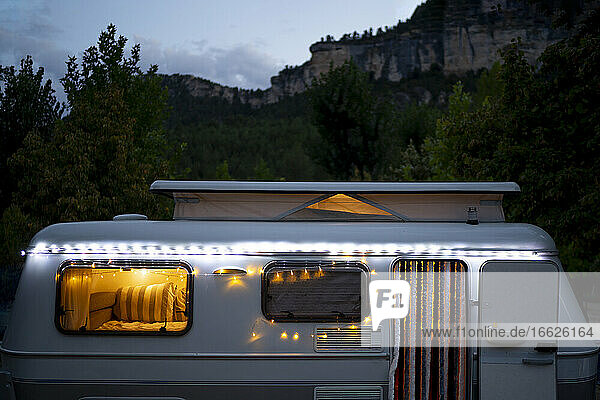 Beleuchtetes Wohnmobil vor einem Berg in der Abenddämmerung