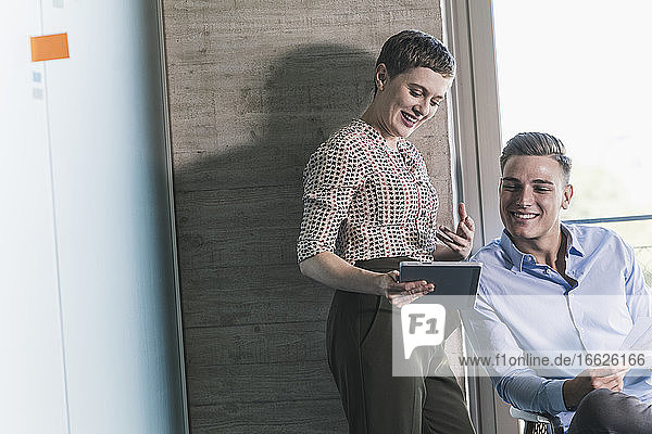 Smiling female entrepreneur discussing over digital tablet with businessman in office