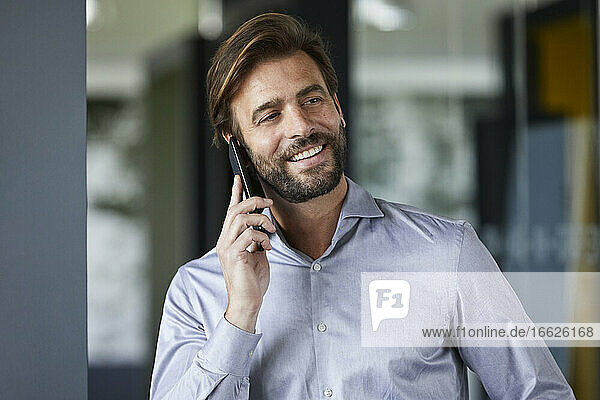 Lächelnder Geschäftsmann  der im Büro mit seinem Handy telefoniert