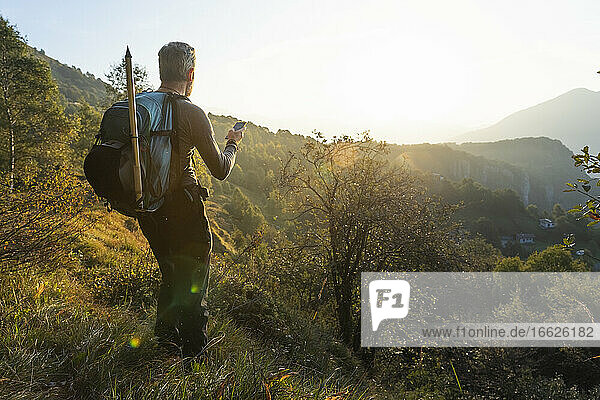 Mature man using smart phone while standing on mountain at sunrise  Orobie  Lecco  Italy