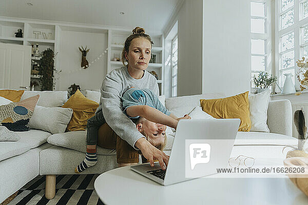 Die Mutter kümmert sich um den Jungen  während sie zu Hause am Laptop arbeitet