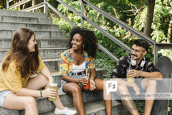 Freunde sitzen auf den Stufen und trinken Saft in einem öffentlichen Park
