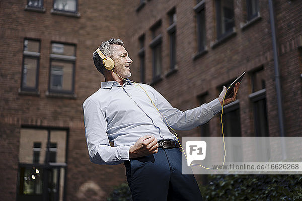 Unbekümmerter Geschäftsmann tanzt beim Hören von Musik gegen ein Gebäude