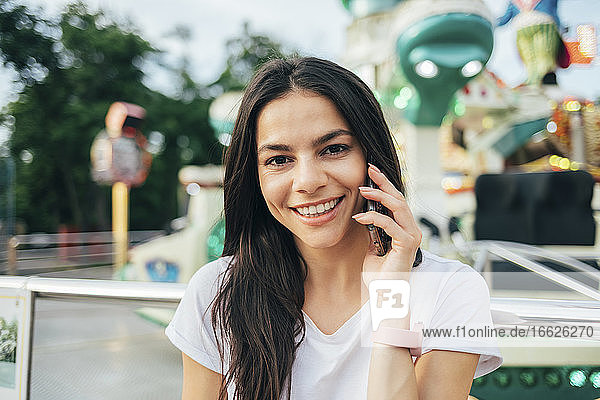 Nahaufnahme einer lächelnden Frau  die in einem Vergnügungspark über ein Smartphone spricht