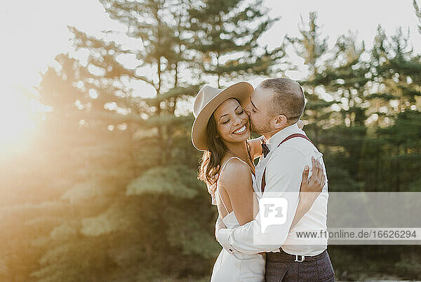 Heterosexual couple kissing while standing in forest during sunset