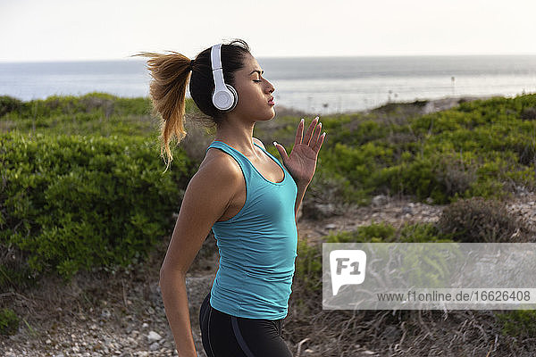 Young Latin woman listening music while jogging near sea