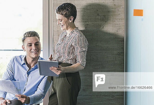Lächelnde Geschäftsfrau  die mit einem männlichen Kollegen im Büro über ein digitales Tablet diskutiert