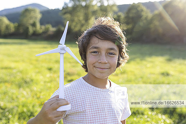 Junge lächelt  während er ein Windrad-Spielzeug auf einer Wiese hält