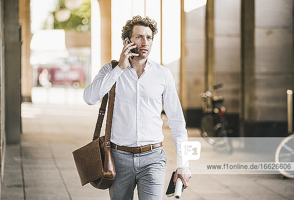 Mann  der beim Gehen an einem Gebäude in der Stadt mit einem Mobiltelefon spricht