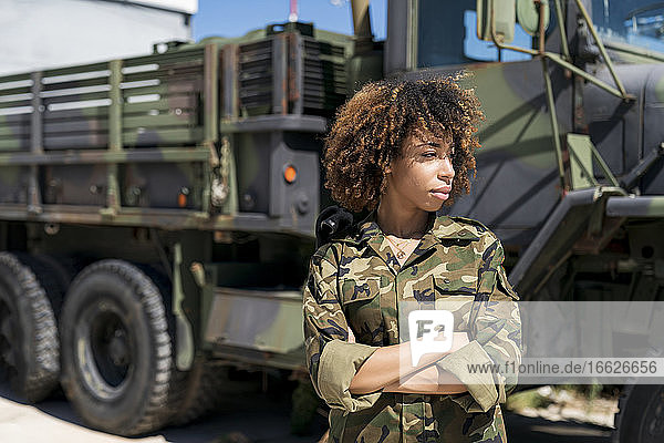 Junge Soldatin mit verschränkten Armen  die wegschaut  während sie an einem Lastwagen auf einem Militärstützpunkt steht