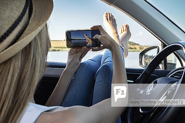 Junge Frau  die im Auto sitzend ihre Füße fotografiert