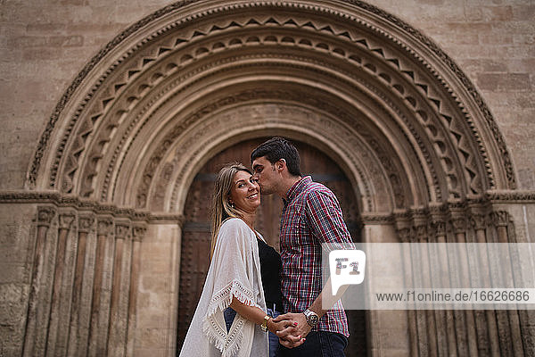 Paar küssen und halten Hand  während gegen Bogen Eingang stehen