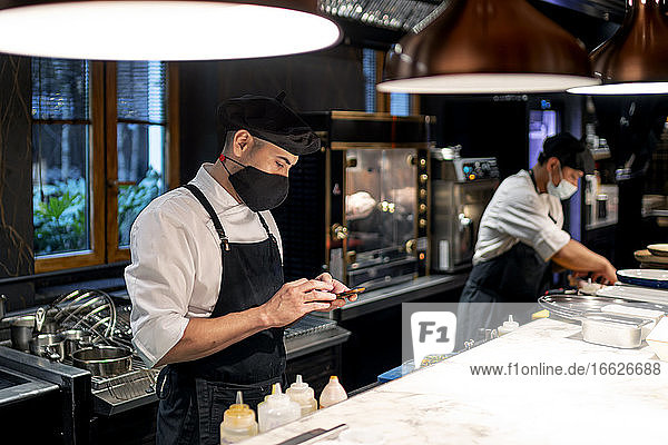 Chefkoch schreibt Textnachrichten auf seinem Smartphone  während er in der Restaurantküche steht