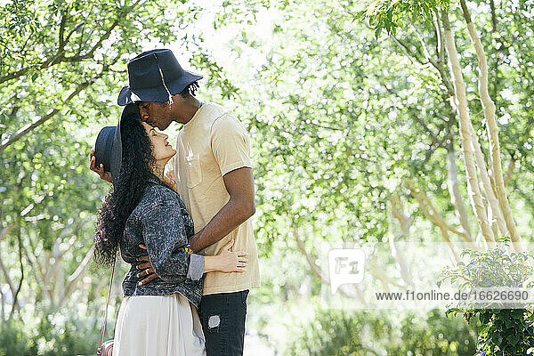 Couple wearing hat kissing while standing at public park