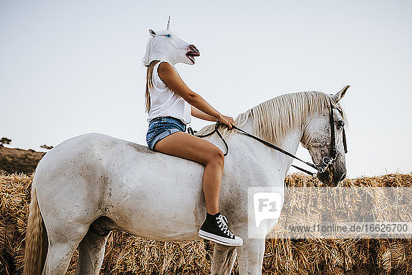 Junge Frau mit Einhornmaske auf dem Pferderücken sitzend