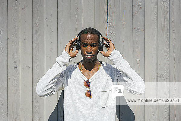 Man adjusting headphones while standing against wall