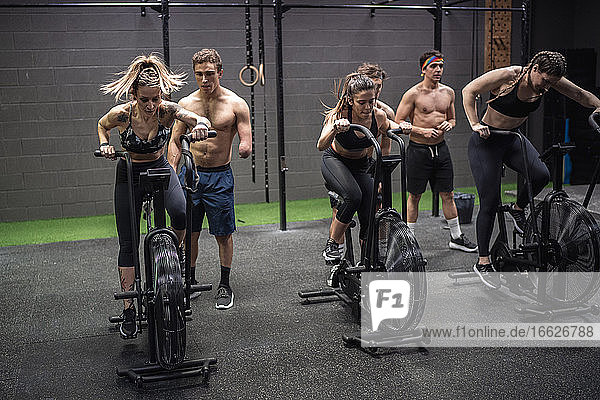 Männer motivieren Frauen  die im Fitnessstudio auf dem Fahrrad trainieren