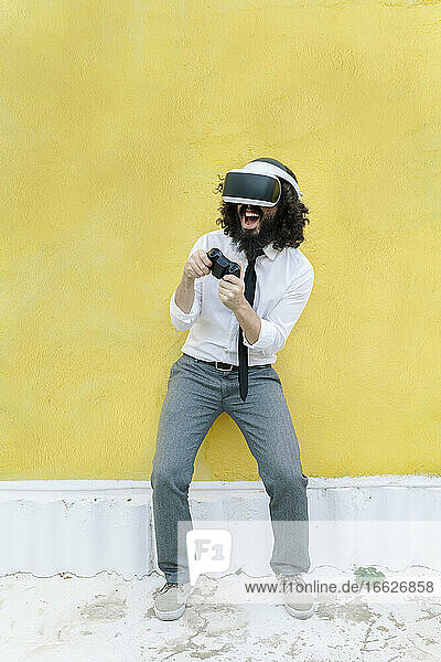 Geschäftsmann mit Virtual-Reality-Brille spielt ein Videospiel  während er an der Wand steht