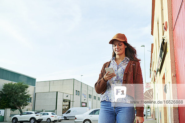 Lächelnde Frau mit Mütze  die ein Mobiltelefon benutzt  während sie in der Stadt steht