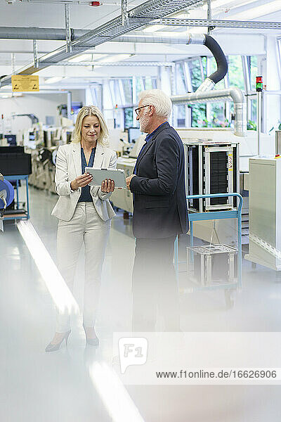 Geschäftsfrau und Geschäftsmann diskutieren über ein digitales Tablet in einer Fabrik