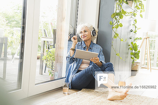 Reife Frau  die wegschaut und Musik hört  während sie an einem digitalen Tablet arbeitet