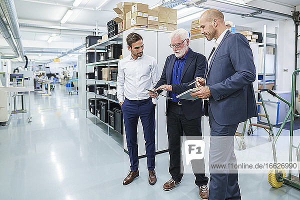 Senior manager discussing over machine part with male colleagues while standing at illuminated factory