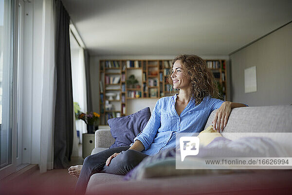 Lächelnde Frau  die wegschaut  während sie zu Hause auf dem Sofa sitzt