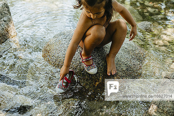 Nettes Mädchen  das im fließenden Wasser spielt  während es im Sommer auf einem Felsen sitzt